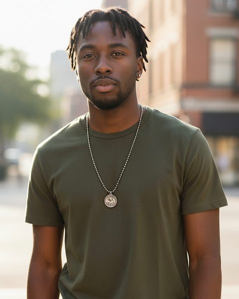 Man wearing a green t-shirt and necklace standing outdoors with a blurred background